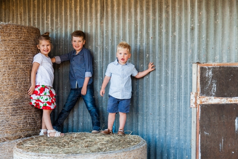 Three happy children on hay bales at farm - Australian Stock Image