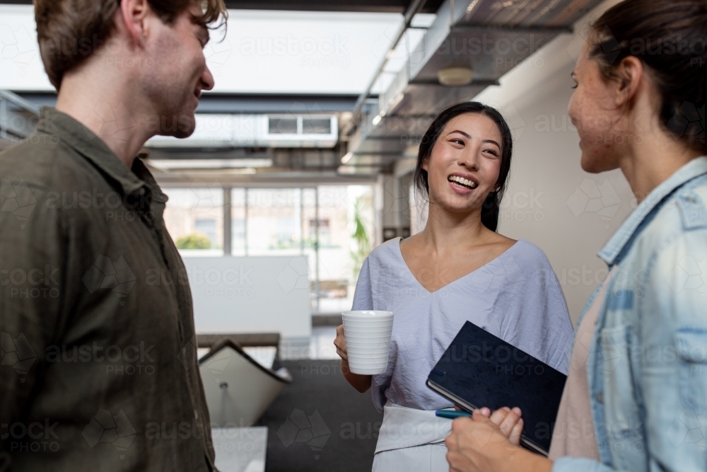 Three happy office workers talking together in an industrial co-working space - Australian Stock Image