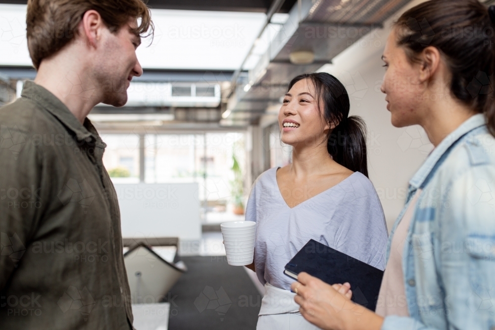 Three happy office workers talking together in an industrial co-working space - Australian Stock Image