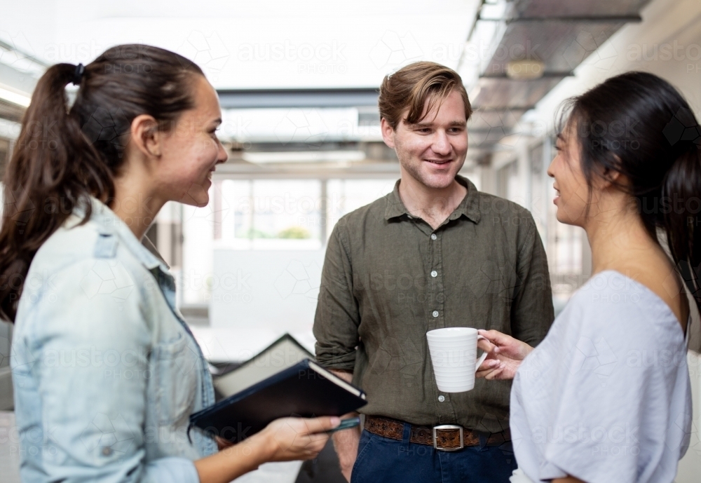 Three happy office workers talking together in an industrial co-working space - Australian Stock Image