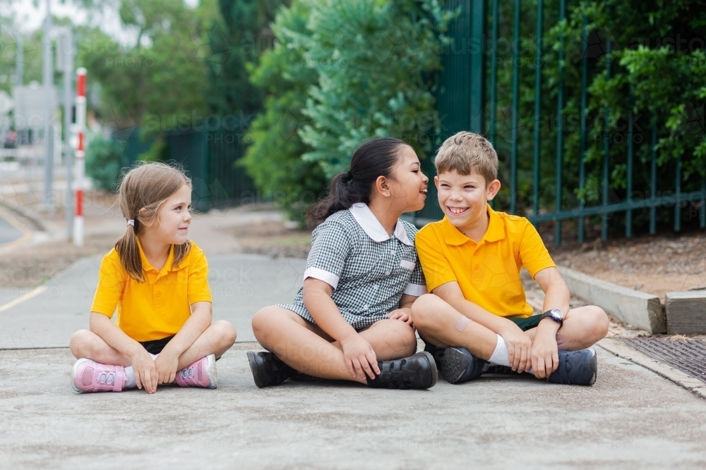 Three happy public school friends in uniform sitting outside - Australian Stock Image