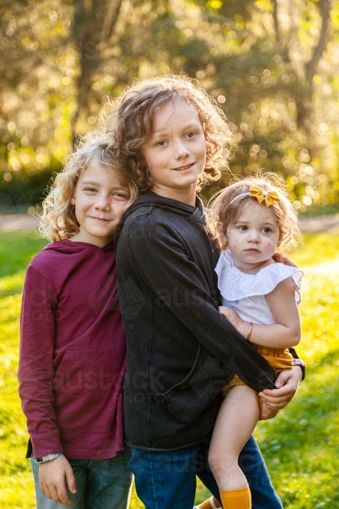 Three happy siblings with curly hair smiling together two boys and a baby girl - Australian Stock Image