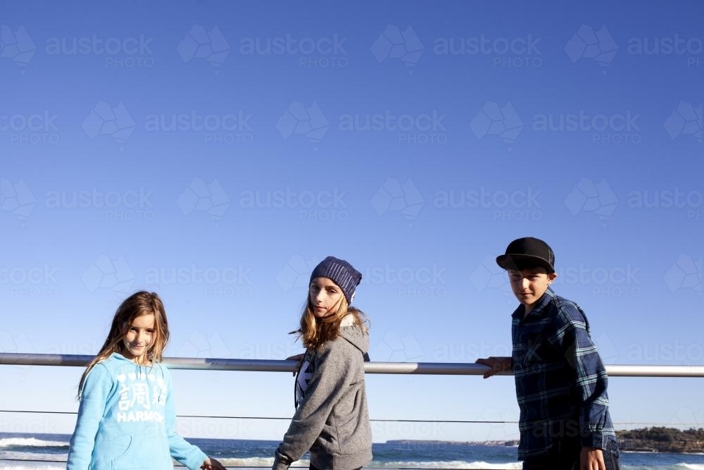 Three kids against a railing in the sunshine - Australian Stock Image