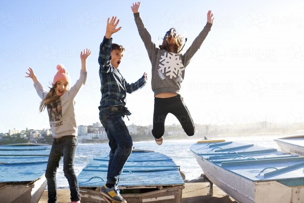 Three kids excitedly jumping in the air off a boat - Australian Stock Image