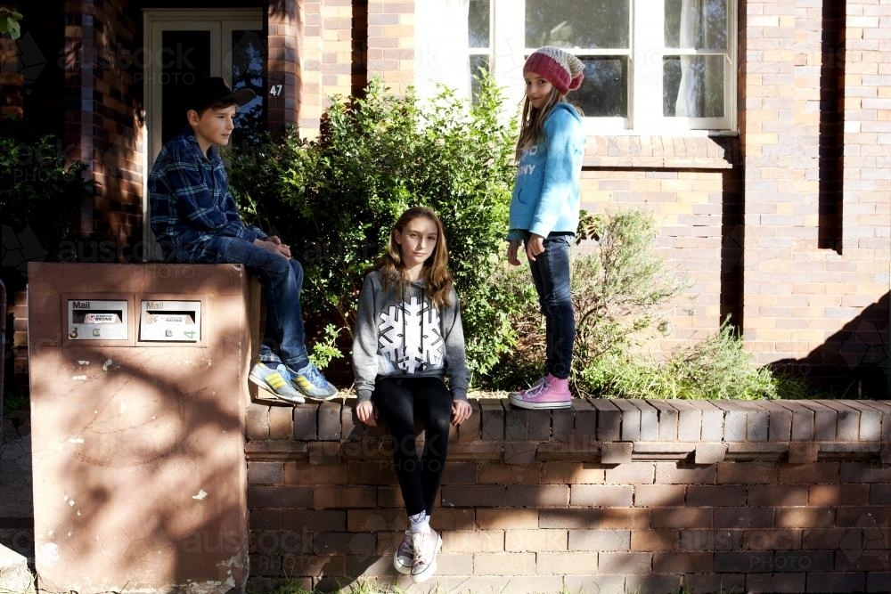 Three kids on the brick wall outside their urban house - Australian Stock Image