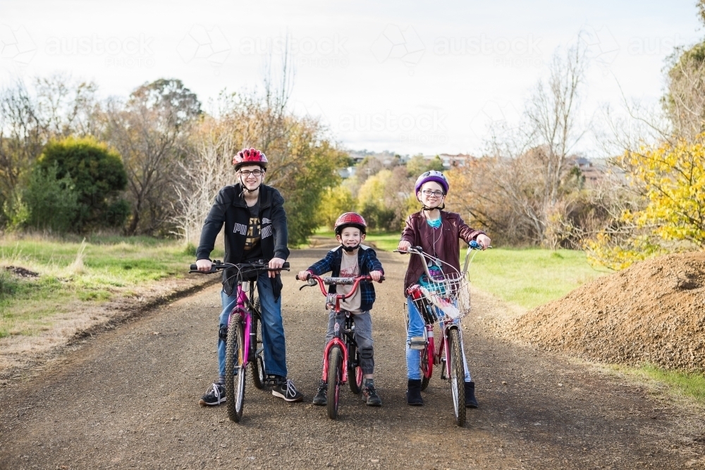 Three kids on their bikes on an unsealed road in park - Australian Stock Image
