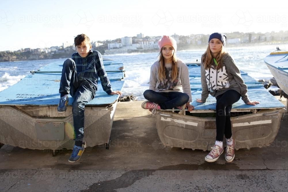 Three kids posing on boats by the ocean - Australian Stock Image
