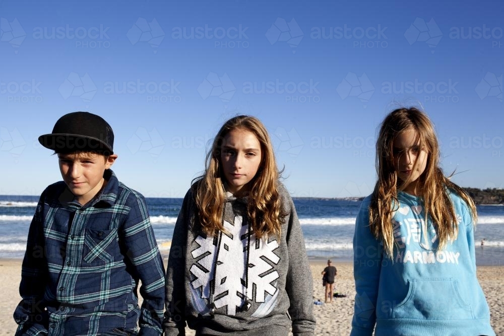 Three kids sitting on a railing in front of the ocean - Australian Stock Image