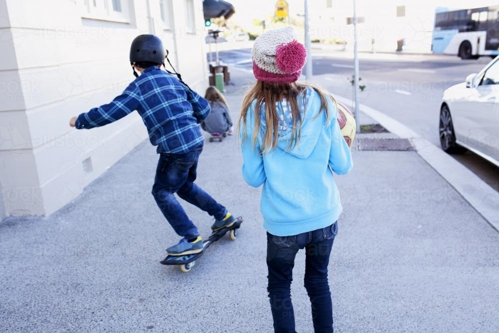 Three kids skating and running down the street - Australian Stock Image