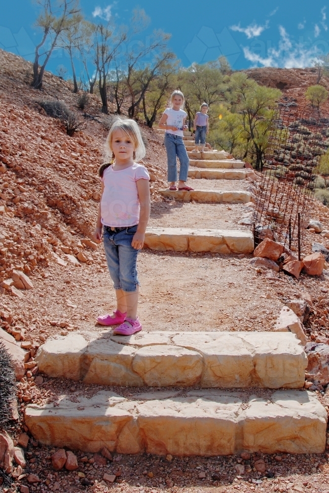Three little girls walking up steps in a hillside in outback Queensland - Australian Stock Image