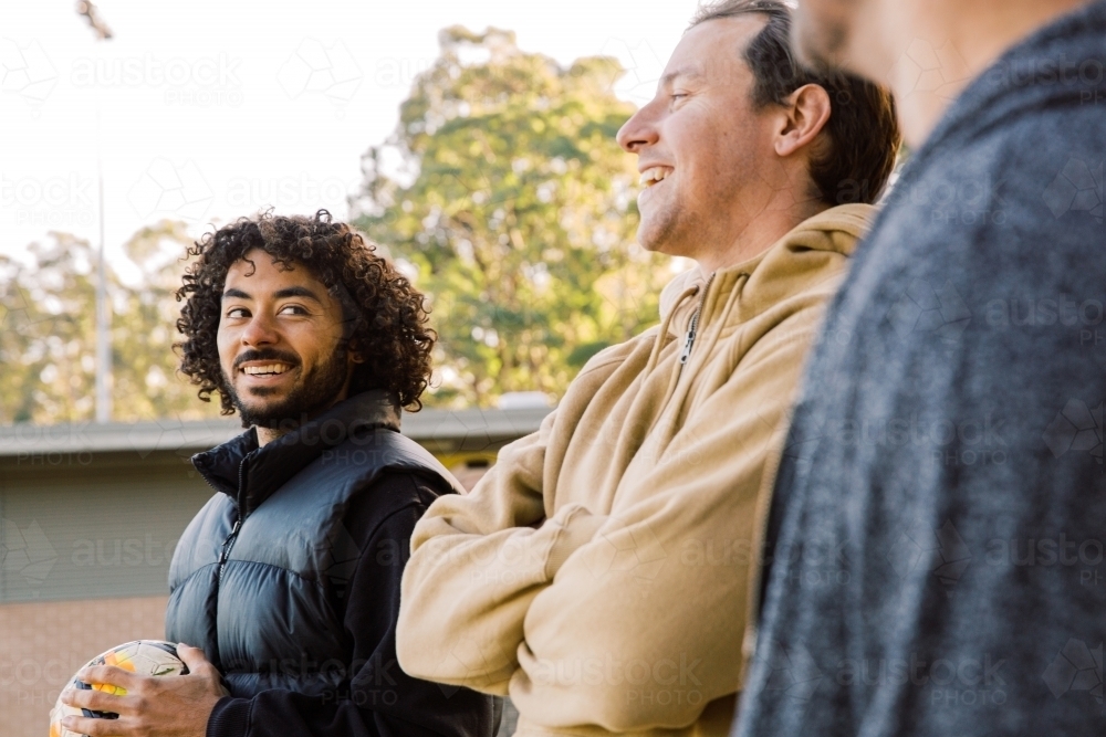 Three men talking and laughing outside one holding a soccer ball - Australian Stock Image