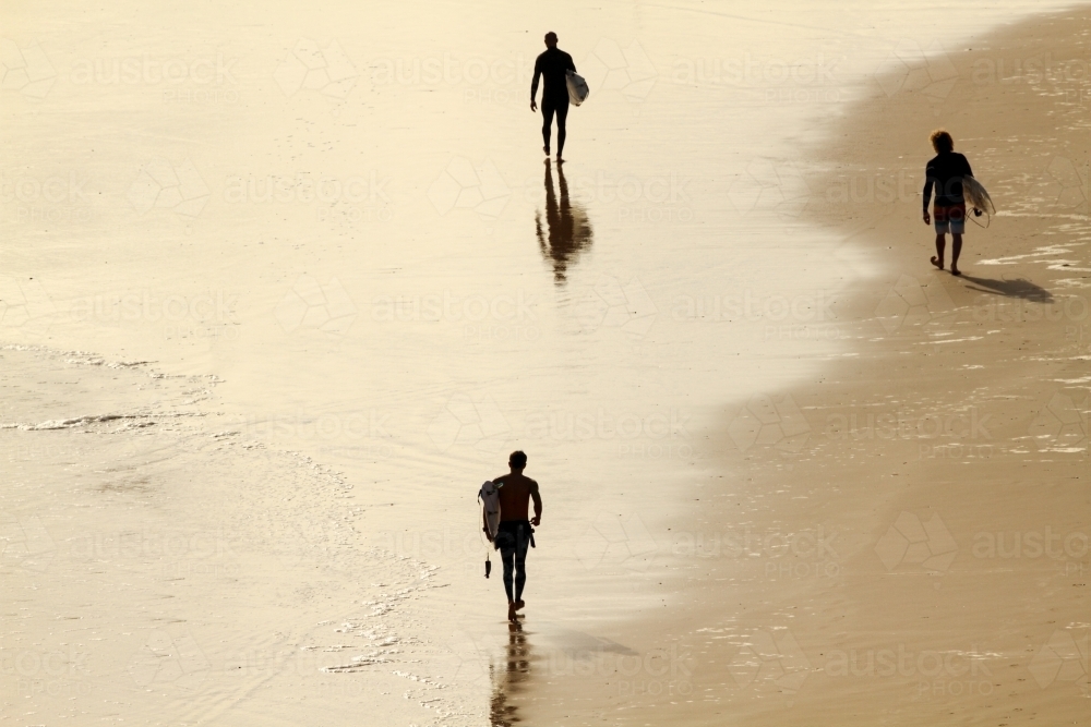 Three men walking along beach with surfboard under their arms. - Australian Stock Image