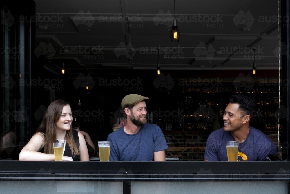 Three people sitting having a drink at a local craft beer bar - Australian Stock Image