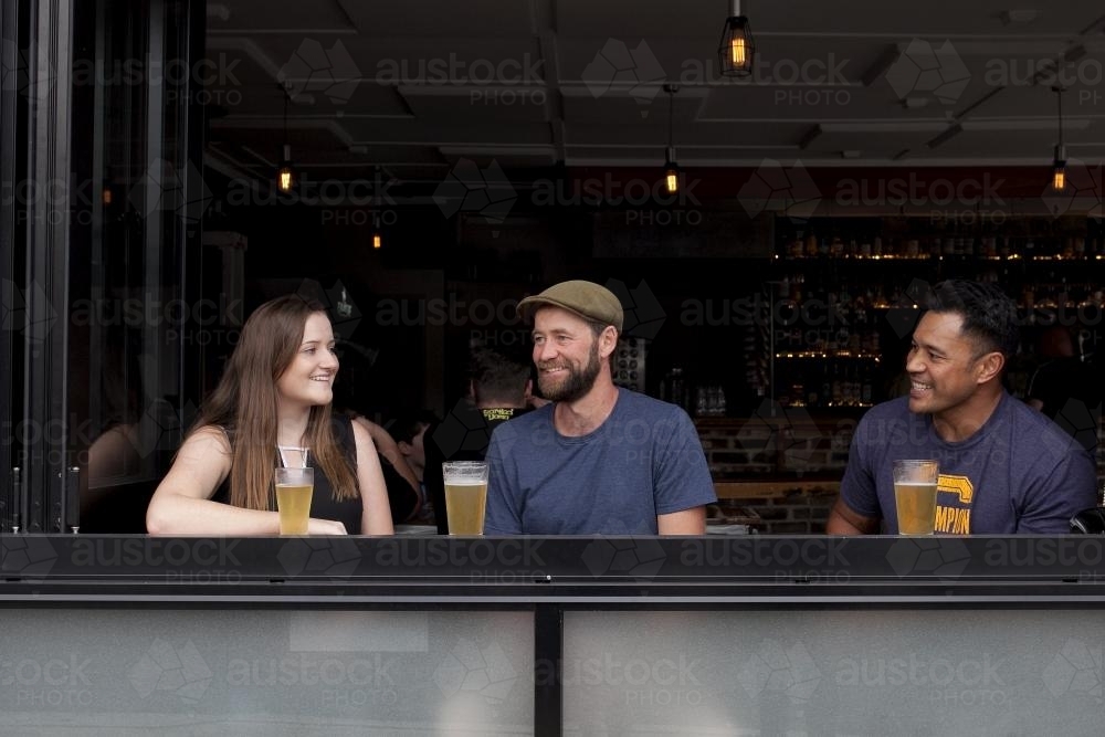 Three people sitting having a drink at a local craft beer bar - Australian Stock Image