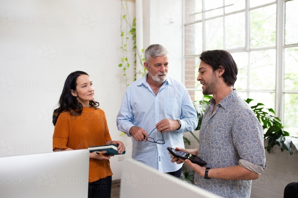 Three people standing, collaborating in an open office - Australian Stock Image