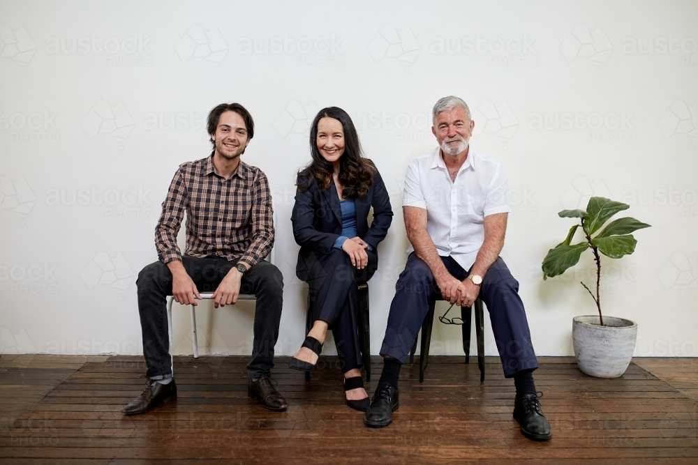 Three professional business people sitting in a row in a studio - Australian Stock Image