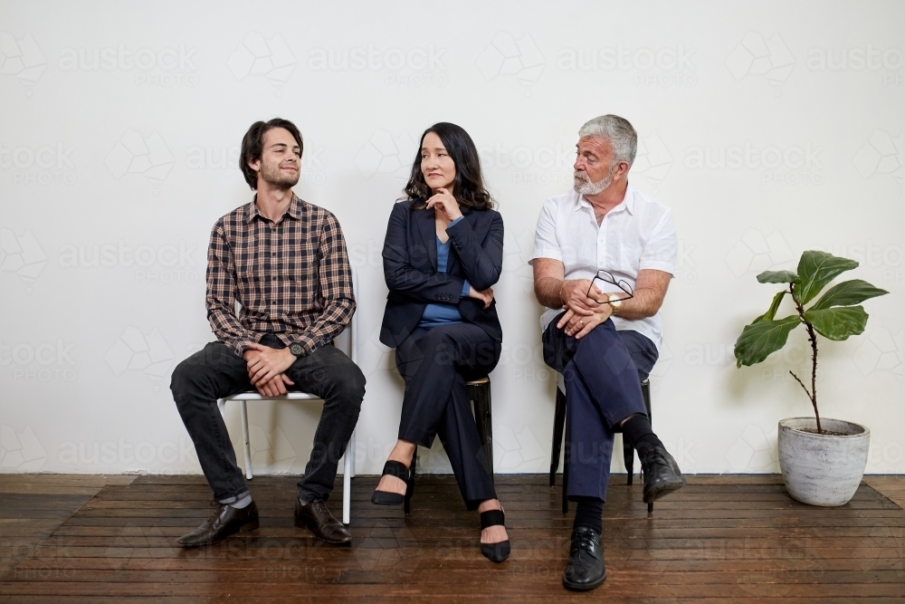 Three professional business people sitting in a row in a studio - Australian Stock Image