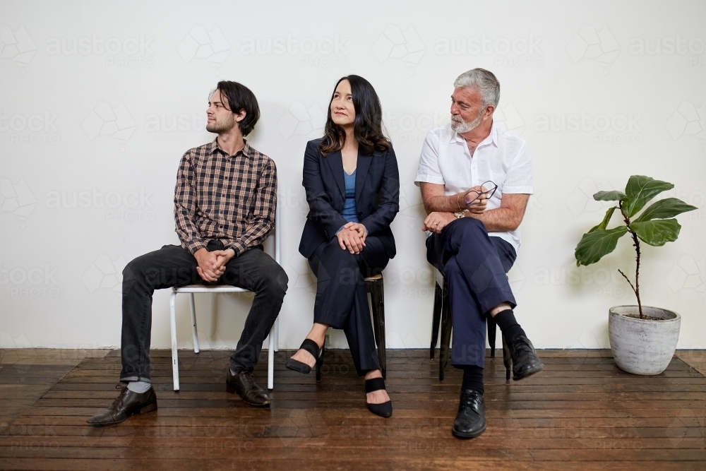 Three professional business people sitting in a row in a studio - Australian Stock Image