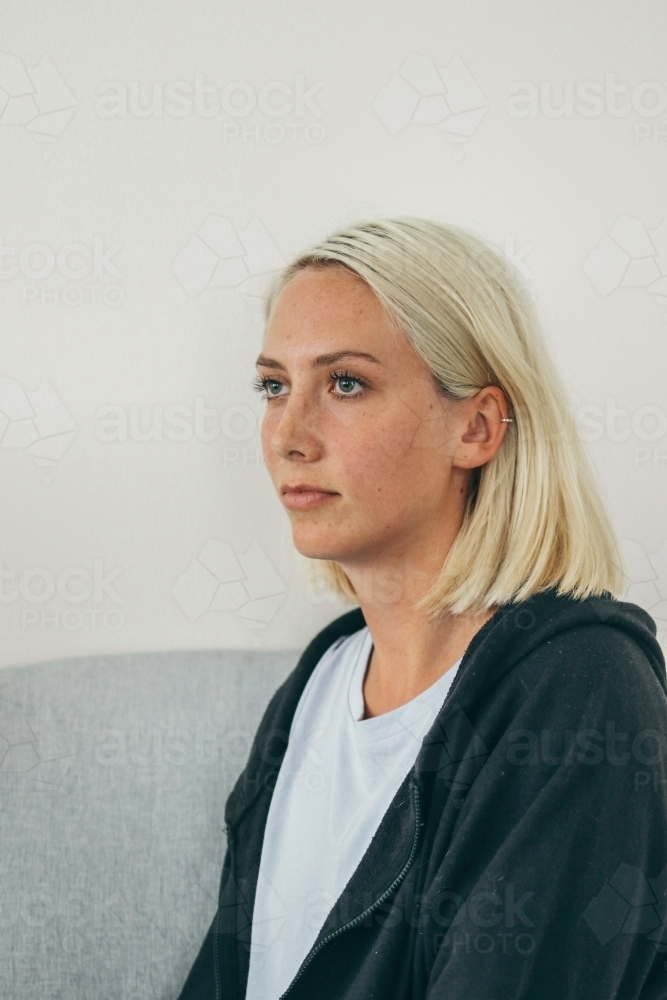 Three quarter profile of young blonde woman in hoodie and t-shirt looking away - Australian Stock Image