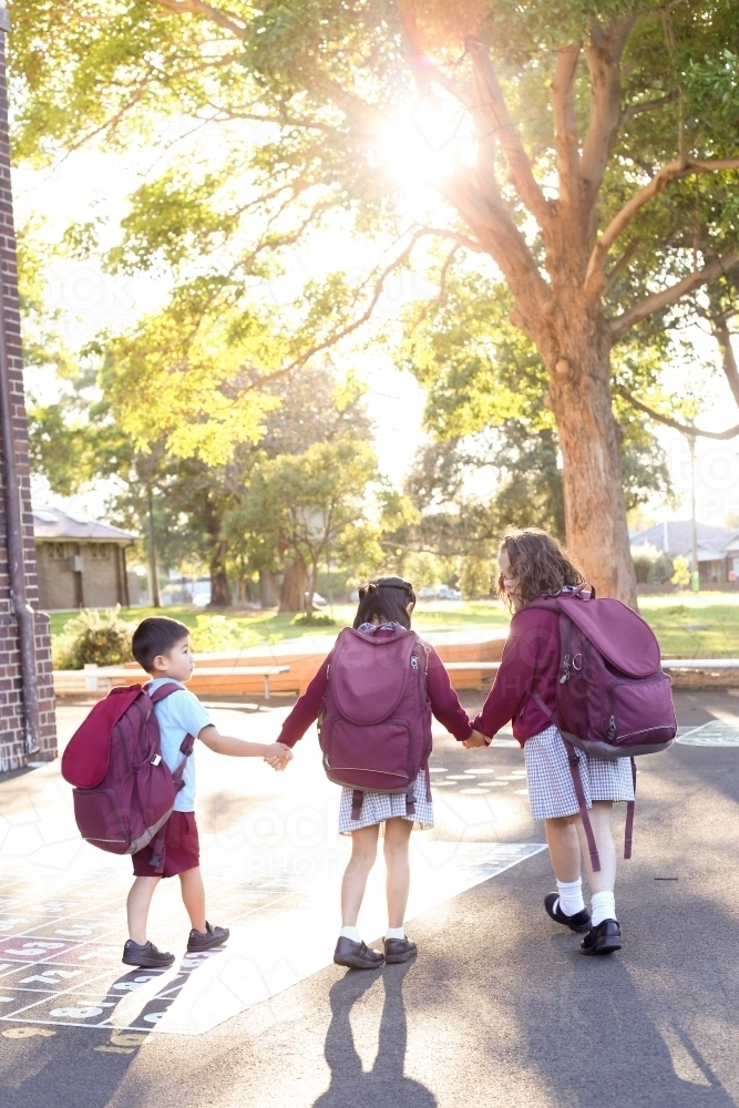 Three school children, holding hands, walking through playground - Australian Stock Image