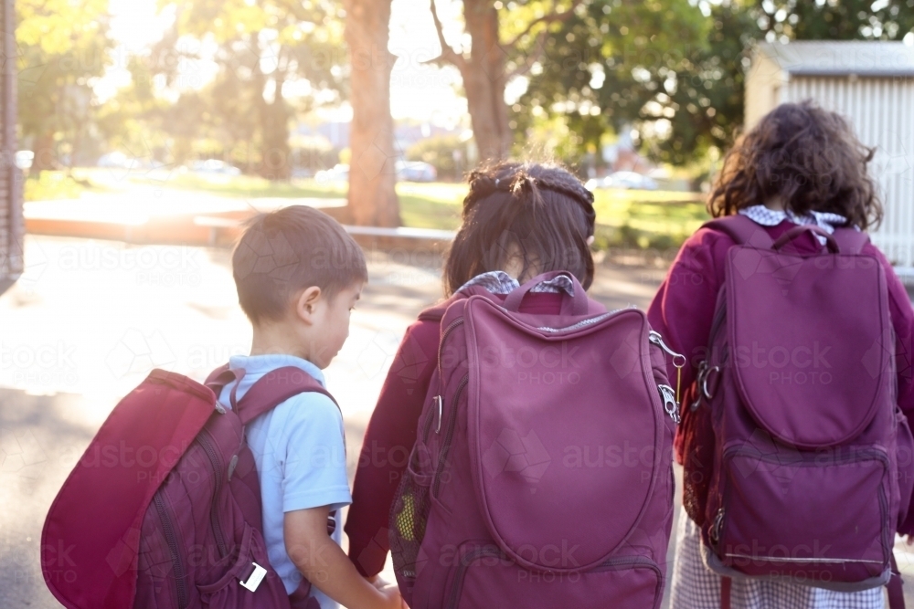 Three school children with backpacks, walking together outside - Australian Stock Image