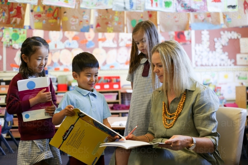 Three school kids showing their work to the teacher in the classroom - Australian Stock Image