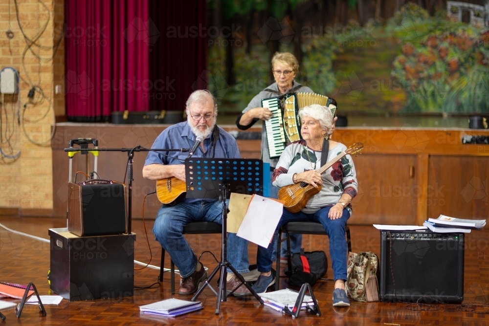 three seniors rehearsing musical piece in a hall - Australian Stock Image