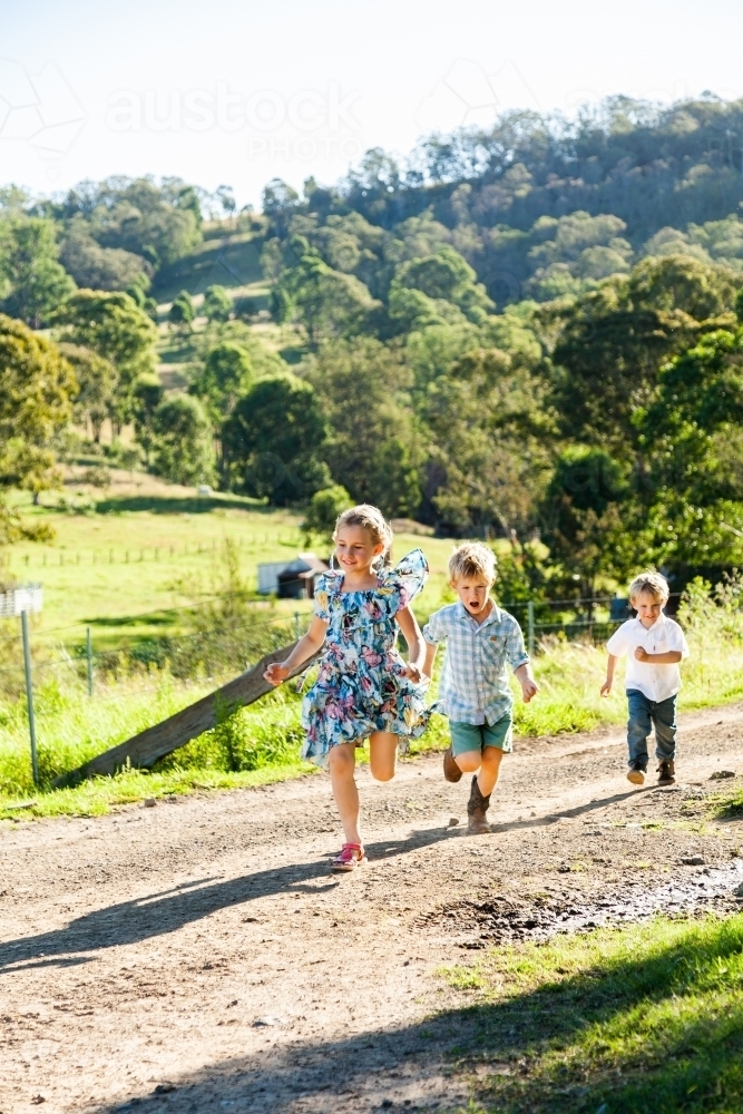 Three siblings running down driveway playing tips - Australian Stock Image