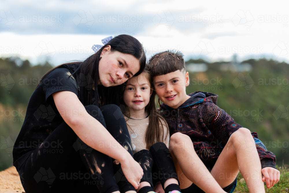 Three siblings sitting together outside in nature - Australian Stock Image