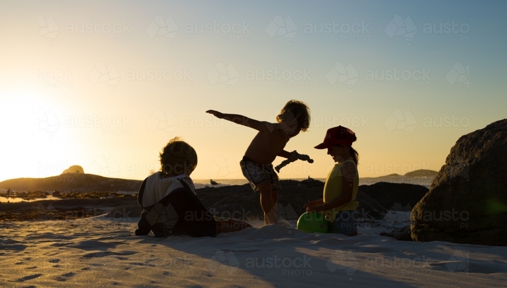 Three silhouette kids playing on the beach at sunset - Australian Stock Image