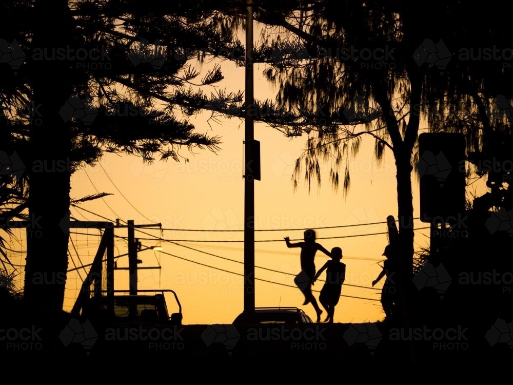 Three silhouetted kids playing in the glow of dusk with power lines - Australian Stock Image