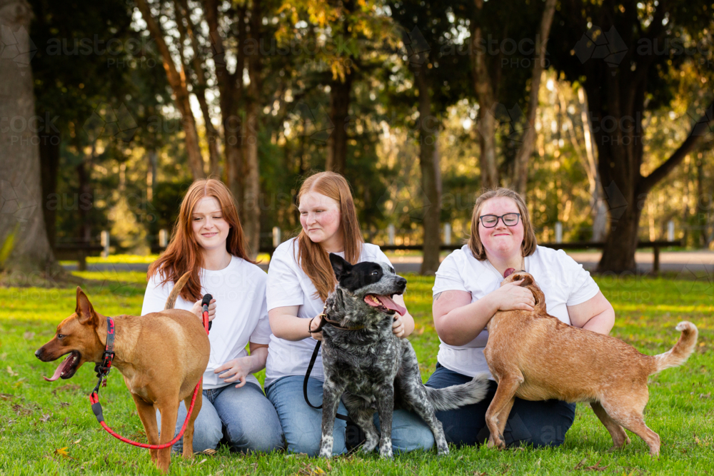 Three sisters and with their Australian cattle dog pets sitting together at park - Australian Stock Image