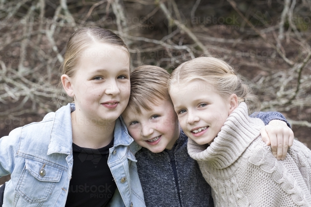 Three smiling siblings hugging outdoors - Australian Stock Image