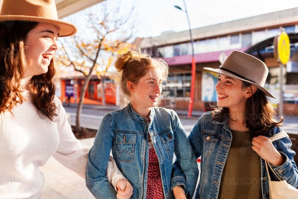 Three teen girls laughing and chatting together while walking down street of town - Australian Stock Image