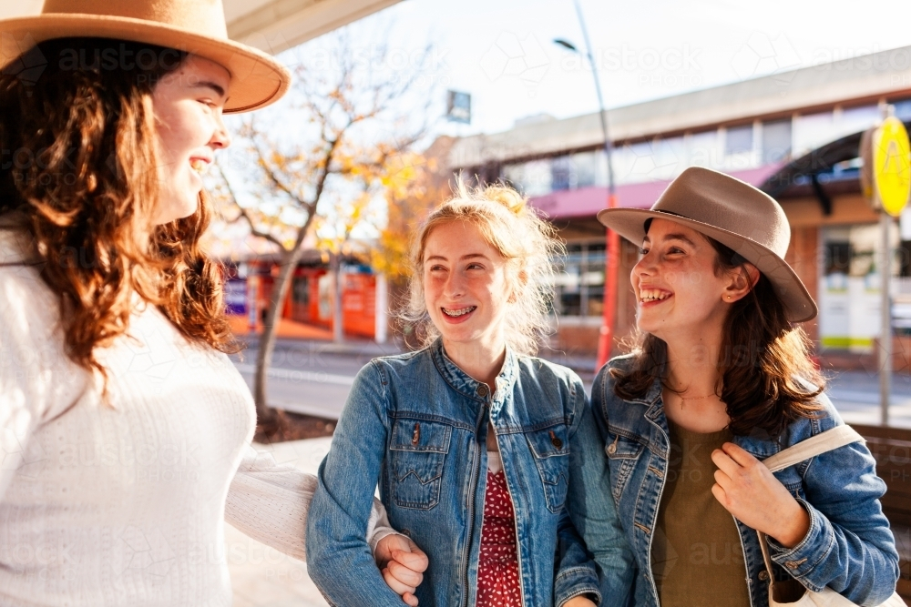 Three teen girls laughing and chatting together while walking down street of town - Australian Stock Image