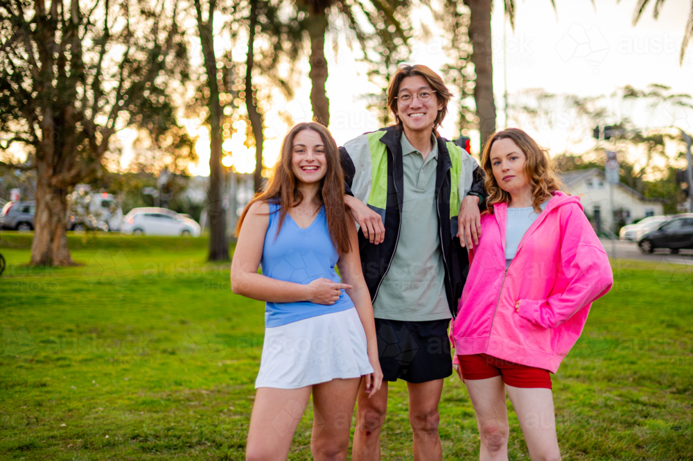 Three teenagers pose together in a park while the sun sets in the background - Australian Stock Image