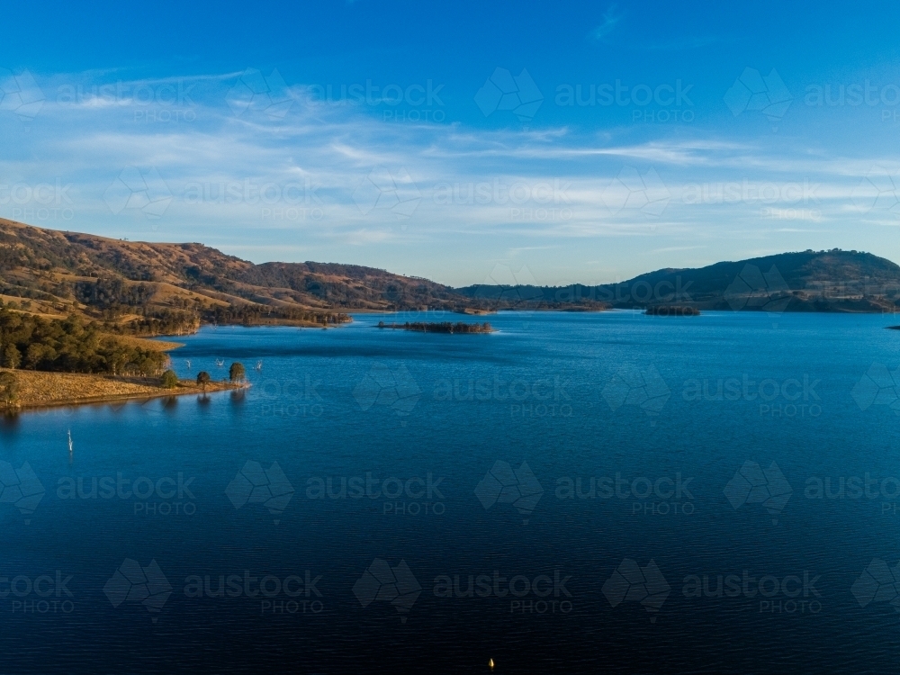 Three trees on sunlit point of land on edge of water catchment lake - Australian Stock Image