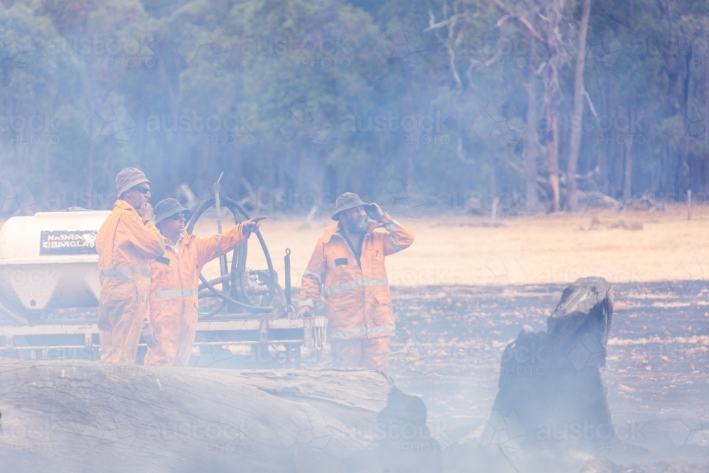 Three volunteer firefighters in smoke surveying the damage after a fire - Australian Stock Image