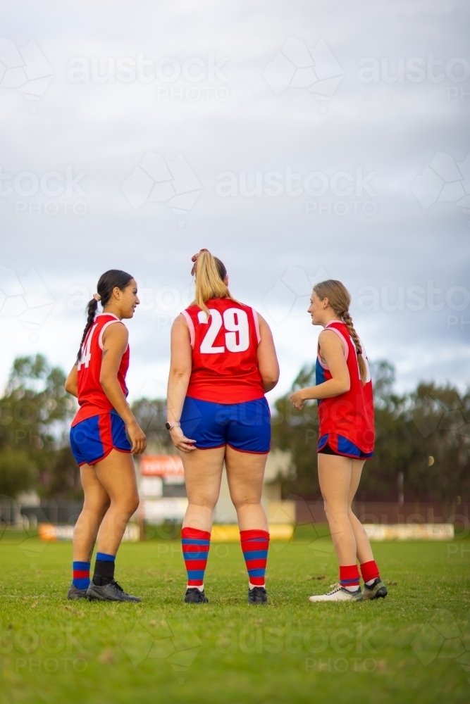 three women football players in red and blue uniforms standing on footy oval - Australian Stock Image
