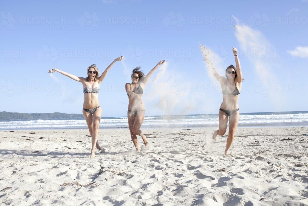 Three women running on beach throwing sand - Australian Stock Image