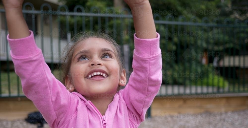 Three Year Old Aboriginal Girl Reaching Up in Playground - Australian Stock Image