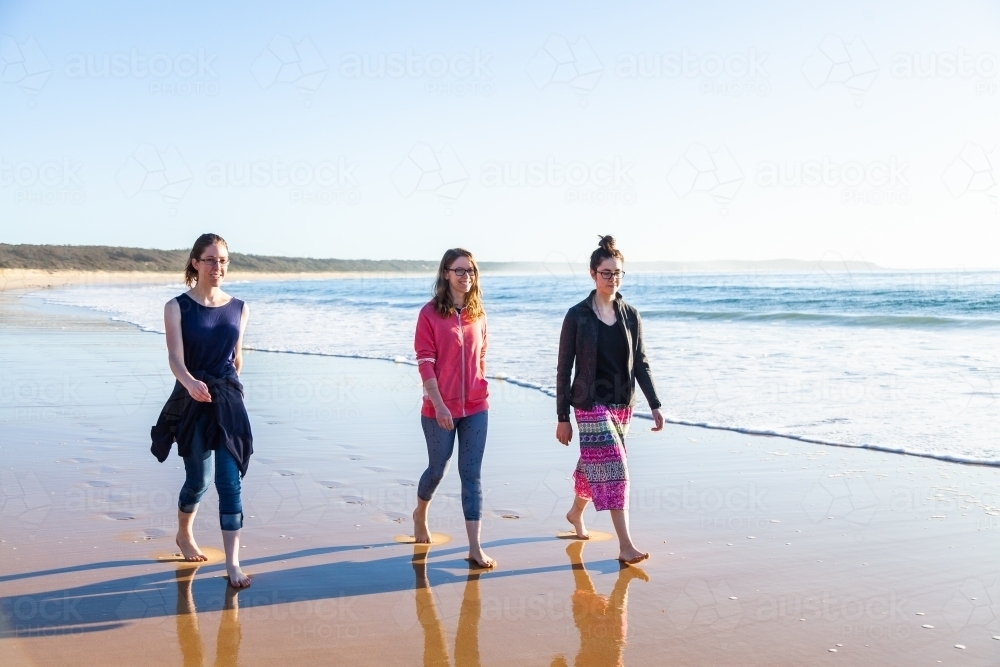 Three young adults walking along the beach seaside scene - Australian Stock Image