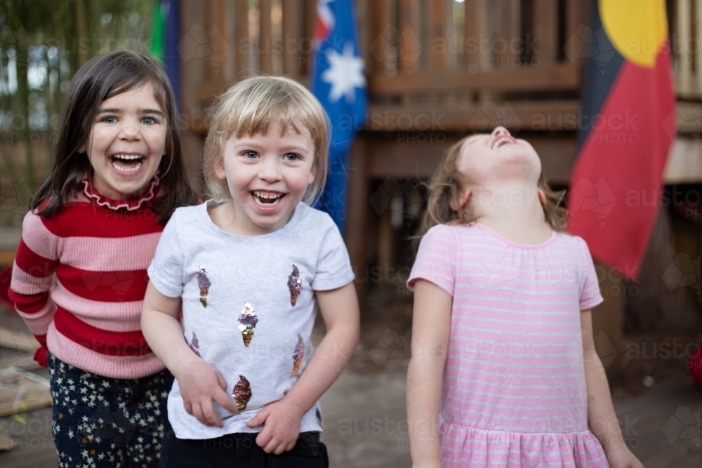 Three young girls laughing together at preschool - Australian Stock Image