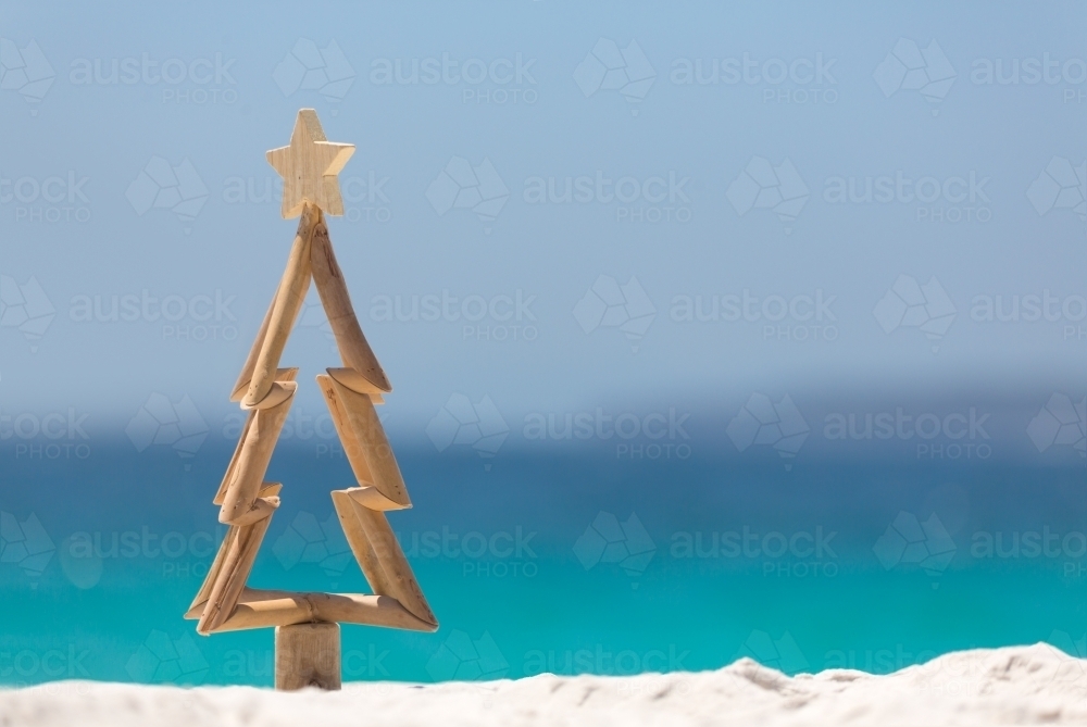 Timber Christmas tree with star sits in pristine white sand with idyllic beach background - Australian Stock Image