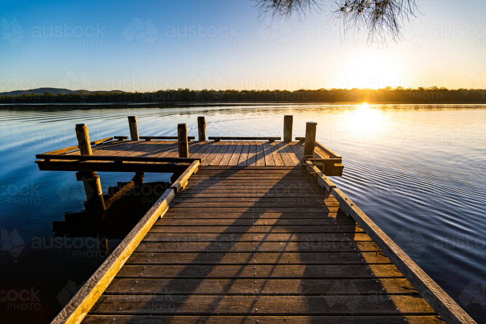 Timber jetty at sunrise beside calm water - Australian Stock Image