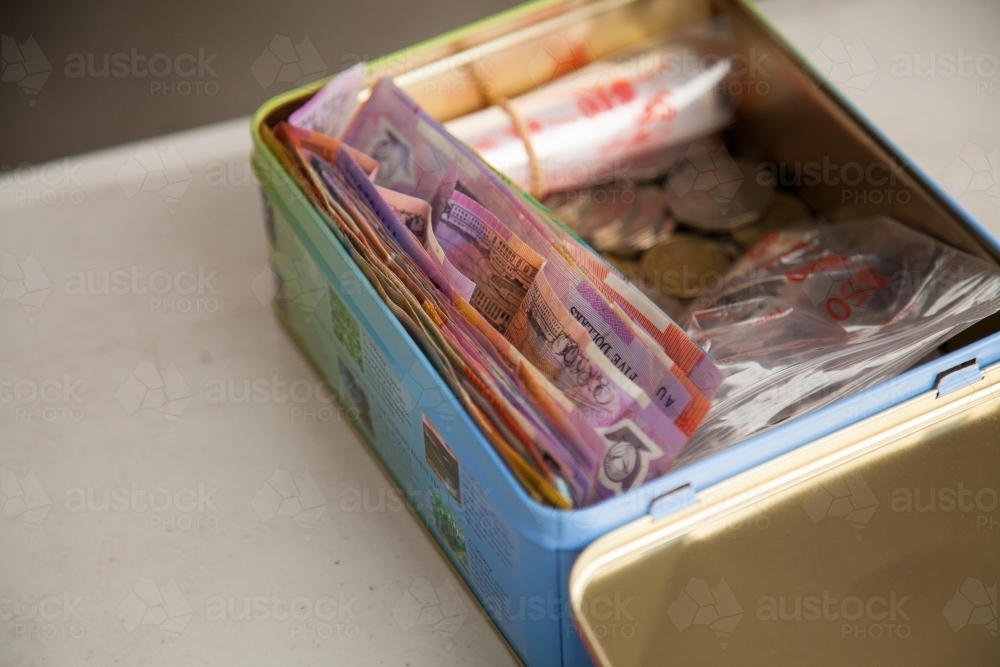 Tin box of money in notes and coins - Australian Stock Image