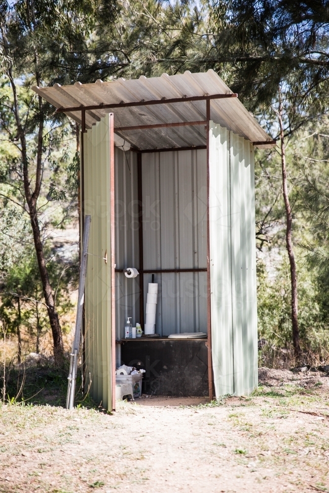 Tin outhouse with long drop toilet on dirt ground with trees - Australian Stock Image