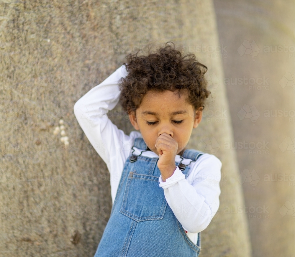 tired young child sucking thumb and twirling hair with eyes closed - Australian Stock Image