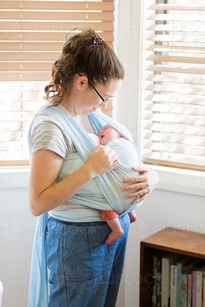Image of Tired young mum carrying sleepy newborn baby in wrap carrier