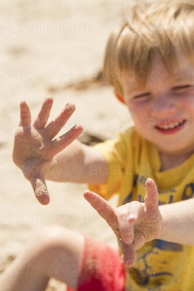 Toddler boy holding out sandy fingers at the beach - Australian Stock Image